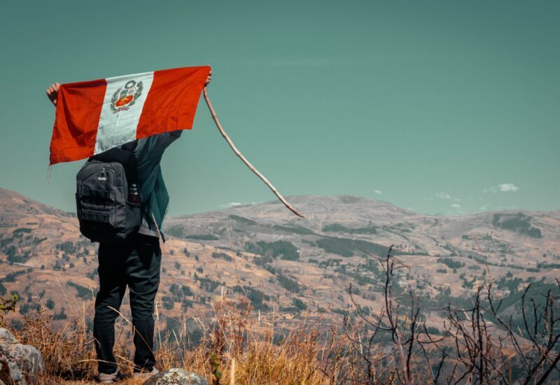 Excursionista de espaldas sosteniendo la bandera de Perú frente a un valle de montaña